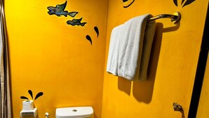 Casa de banho com parede amarela, sanita, porta-toalhas com toalha e rolo de papel higiénico.