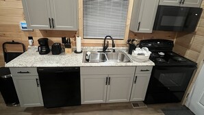 A compact kitchen with a granite countertop, stainless steel sink, black dishwasher, and a black stove. - Lillie's Pad -Cozy 2-bedroom cabin- 20 miles from Natural Bridge in Beattyville. (Beattyville)