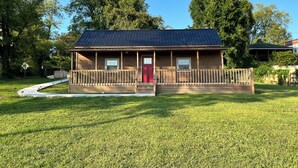 A wooden cabin with a red door, a porch, and a metal roof. - Lillie's Pad -Cozy 2-bedroom cabin- 20 miles from Natural Bridge in Beattyville. (Beattyville)