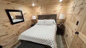 A wooden-paneled room with a bed, two bedside lamps, a mirror, and a bench. - Lillie's Pad -Cozy 2-bedroom cabin- 20 miles from Natural Bridge in Beattyville. (Beattyville)