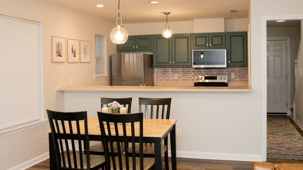 Una cocina moderna con armarios verdes, electrodomésticos de acero inoxidable y una mesa de comedor de madera con sillas.