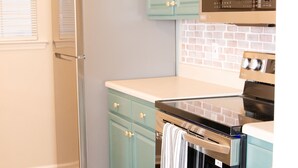 Una cocina con gabinetes color turquesa, un refrigerador de acero inoxidable y un horno negro.