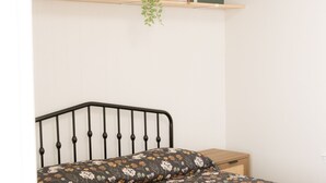 Un dormitorio con una cama, una mesita de noche, un estante con fotos enmarcadas y una planta colgante.