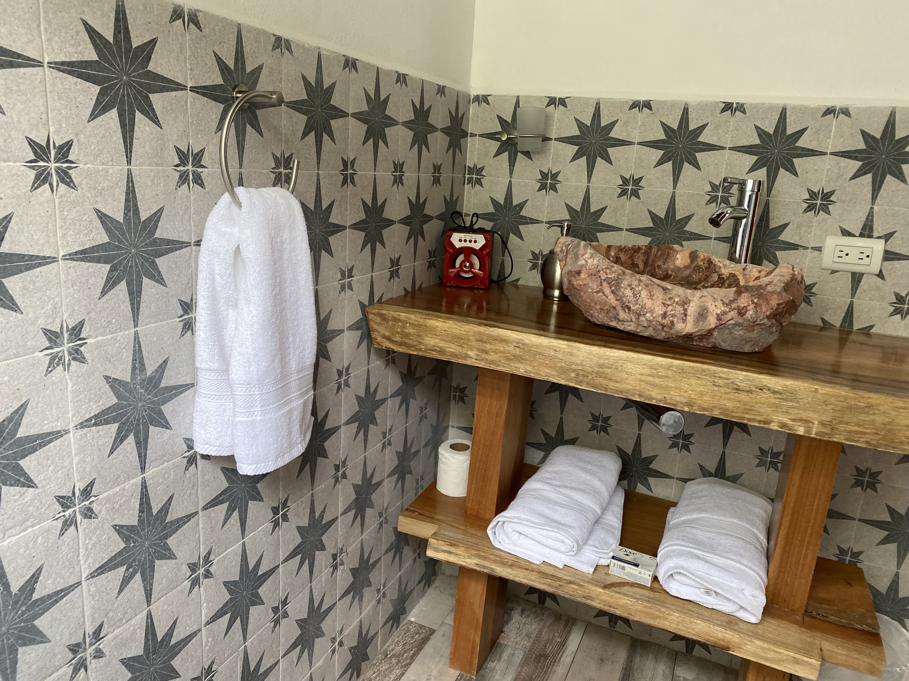 A bathroom with star-patterned tiles, a wooden vanity with a sink, a towel rack, and a shelf with folded towels.