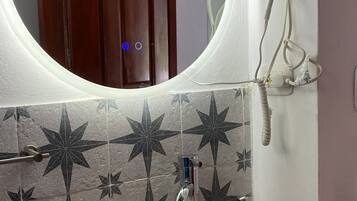 Un baño con lavamanos de piedra, un espejo con luz, un secador de pelo y un rollo de papel higiénico.