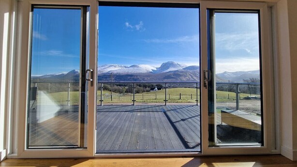 A room with a large sliding glass door leading to an outdoor deck with a view of mountains. - Aonach View near Fort William (Highland Council)