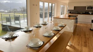 A modern kitchen with a long wooden table set for dining, large windows, and a view of the outdoors. - Aonach View near Fort William (Highland Council)