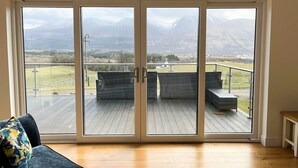 A room with a large sliding glass door leading to an outdoor deck with wicker furniture and a view of mountains. - Aonach View near Fort William (Highland Council)