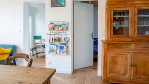 Un salon comprenant une table à manger en bois, un canapé bleu, un meuble en bois et une étagère murale remplie de livres, ainsi qu’une affiche « PORNIC ».
