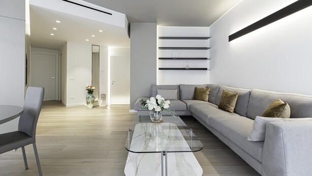 Una sala de estar moderna con un sofá gris, una mesa de centro de vidrio y un jarrón con flores blancas.