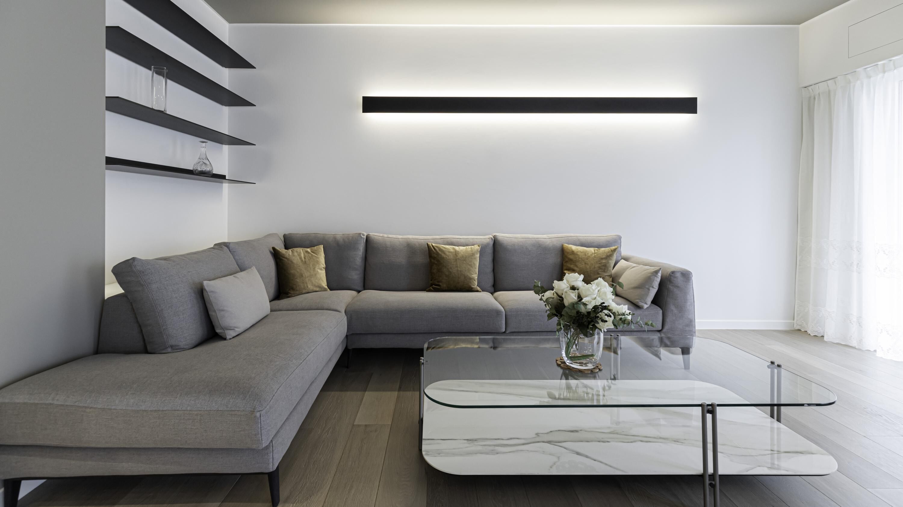 A modern living room with a grey sectional sofa, a glass coffee table, and a minimalist design.
