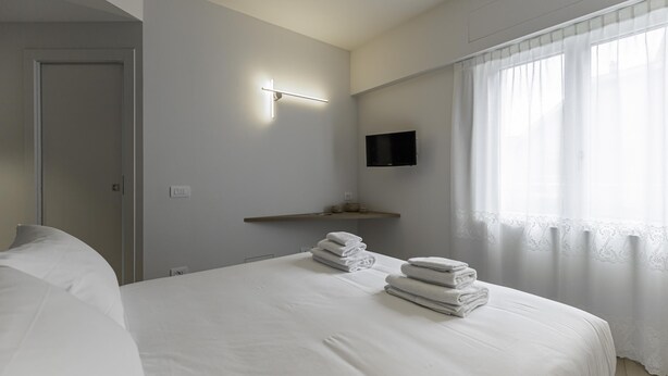 Een moderne hotelkamer met een net opgemaakt bed, een wandtelevisie en een raam met dunne gordijnen.