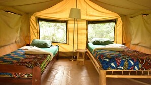 A tent with two beds, each with a patterned bedspread and pillows, a small stool, and a floor lamp. - Room in B&B - Red Rocks Rwanda - Safari Tent Twin (Nkotsi)