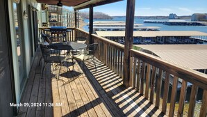 A wooden deck with outdoor furniture, a grill, and a view of a marina and buildings across the water.