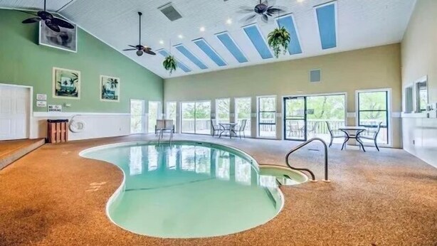 A spacious indoor pool area with a curved pool, ceiling fans, and large windows allowing natural light.