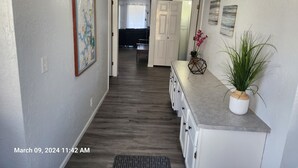 A hallway with a map, a plant, and a door leading to a living area.