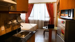A compact kitchen with a sink, stove, and refrigerator. There is a dining table with a chair and a window with curtains. - The Green View Thai Van Lung  (Ho Chi Minh City)