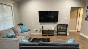 A living room with a grey sofa, a black rug, and a flat-screen TV mounted on the wall. - Charming 3BR Retreat Near Tyler Airport & Downtown (Tyler)