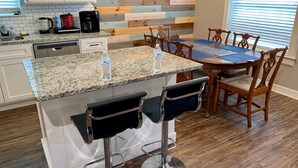 A kitchen with a granite countertop, wooden bar stools, a dining table with chairs, and a wooden backsplash. - Charming 3BR Retreat Near Tyler Airport & Downtown (Tyler)