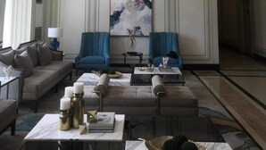 Una hall d'hotel moderna con un grande dipinto astratto, due poltrone blu, una divano e un lampadario originale.
