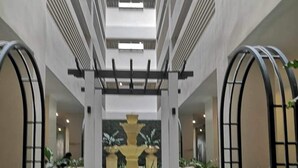 Un ampio atrio con fontana centrale, circondato da piante in vaso e architettura moderna.