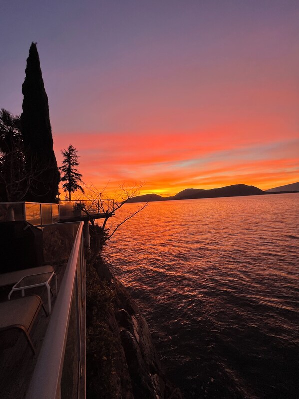 A sunset view over a body of water with a rocky shoreline and a few trees.