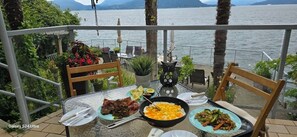 A dining table with plates of food, a black pan, and a decorative owl statue on a balcony overlooking a body of water.