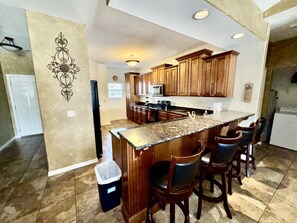 A kitchen with wooden cabinets, a granite countertop, and a bar area with stools.
