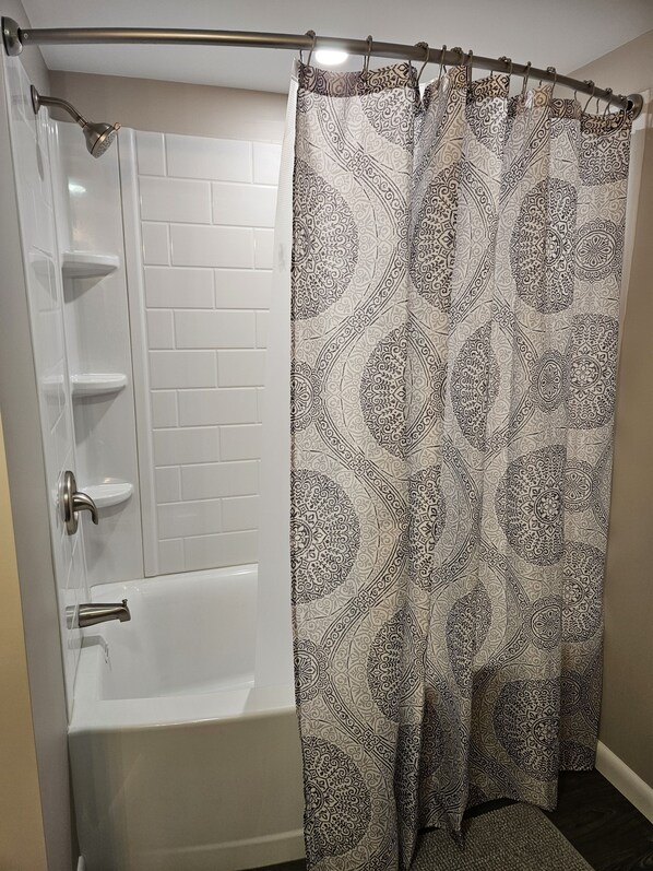 A bathroom with a white bathtub, a shower, and a patterned shower curtain. - Comfortable, spacious home near Knoebels. (Catawissa)