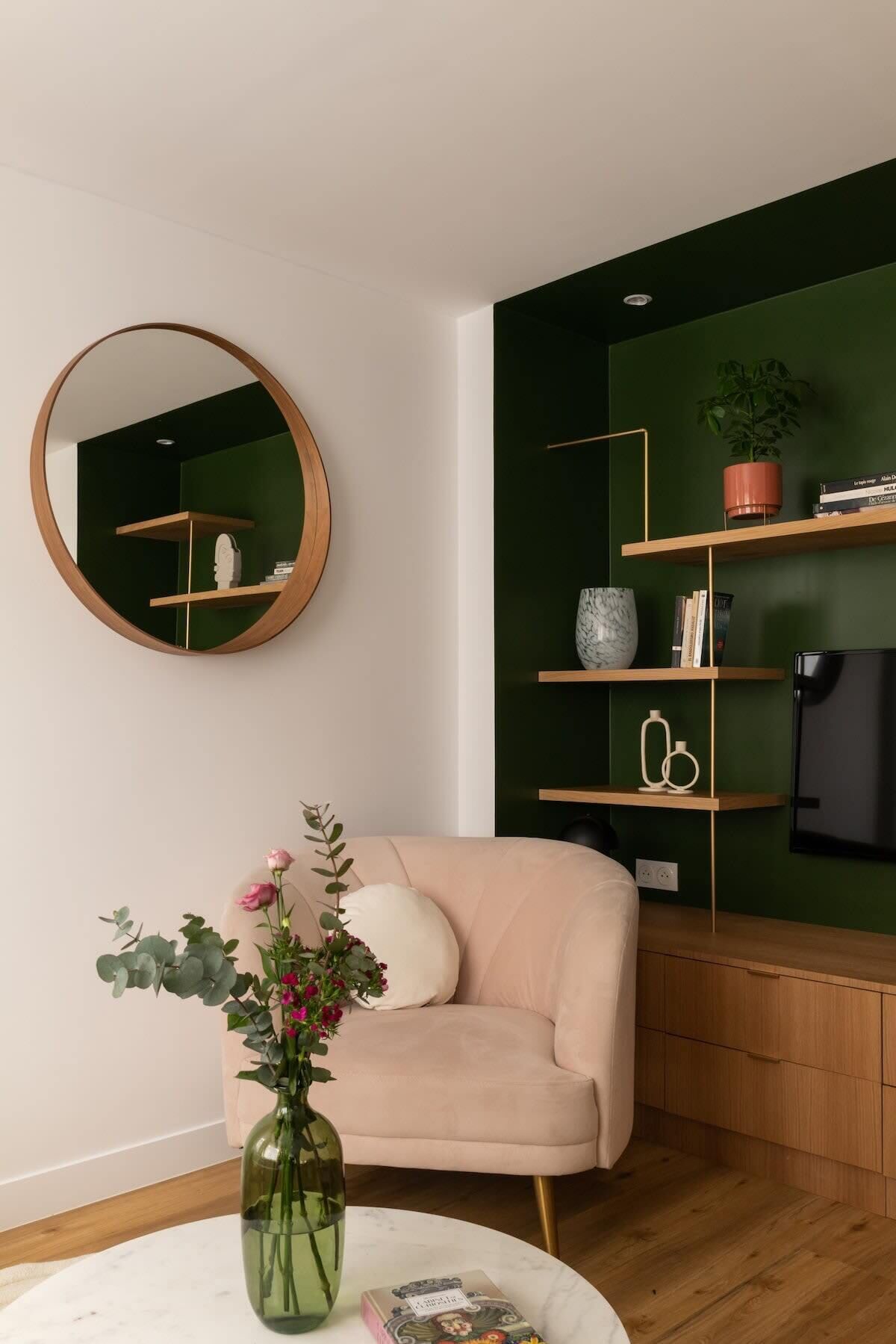 Una sala de estar con un espejo redondo, un sofá color beige, un mueble de madera y una pared verde.
