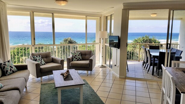 Een ruim balkon met uitzicht op de oceaan, voorzien van twee banken en een salontafel.