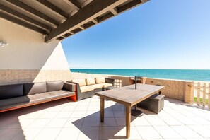 Une terrasse avec un canapé, une table et un barbecue, donnant sur une plage.