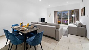 A modern living room with a dining area, grey sofas, and a city view through large windows.