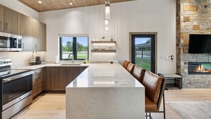 A modern kitchen with a large island, built-in appliances, and a stone fireplace.