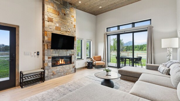 A spacious living room with a stone fireplace, comfortable seating, and large windows offering a view of the outdoors.
