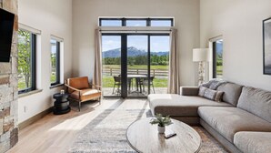 A spacious living room with a large sliding glass door leading to an outdoor area, a sofa, a chair, and a coffee table.