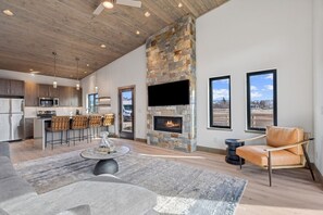 A modern living room with a stone fireplace, a bar area, and a large TV mounted on the wall. - Mara Luxury Cabin- Aspen (Hamilton)