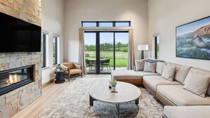 A spacious living room with a stone fireplace, a large sofa, a round coffee table, and a television mounted on the wall. - Mara Luxury Cabins- Pine (Hamilton)