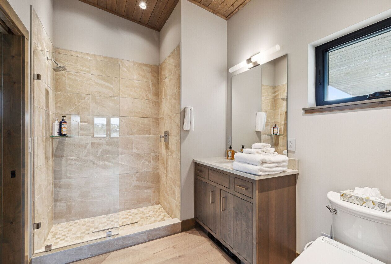 Un bany modern amb dutxa protegida per vidre, un lavabo amb mirall i un vàter.