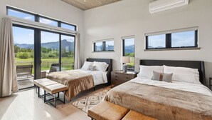 Una habitación de hotel moderna con dos camas, un amplio ventanal corredero que da a un balcón y vistas a las montañas.
