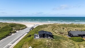Una proprietà costiera con una strada che conduce a una spiaggia, caratterizzata da case moderne con ampie finestre e vista sull'oceano.