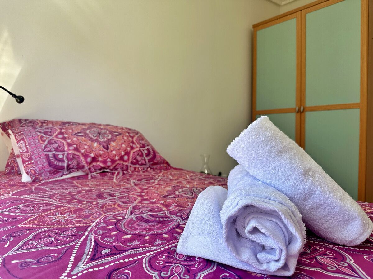 A bed with a patterned bedspread and two rolled towels.