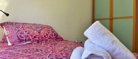 A bed with a patterned bedspread and two rolled towels.