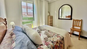 Un dormitorio con cama, una silla, un espejo y una ventana con cortinas.
