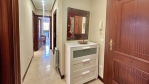 Un pasillo con una puerta de madera, un mueble blanco con cajones y un radiador en el suelo.