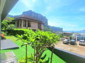 Enjoy a serene view of the surrounding mountains and coastline from this balcony, overlooking a lush garden and parking area.