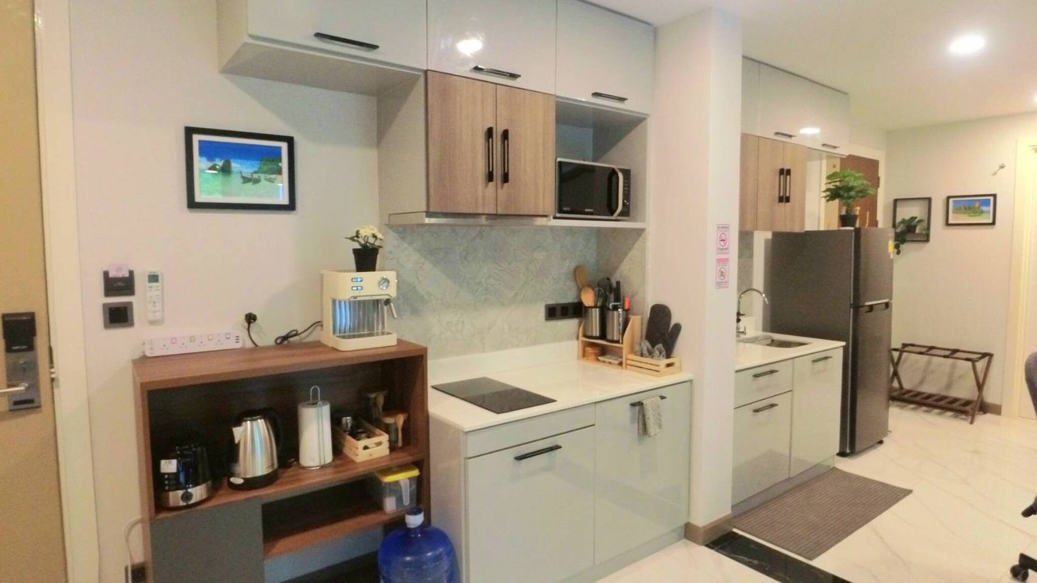 A modern kitchen with light-colored cabinets, a built-in microwave, a coffee machine, and a water dispenser.