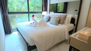 Relax in a spacious room with a large bed and a window offering a view of lush greenery.