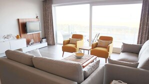 Un salon moderne avec un canapé, deux fauteuils, une table basse et un téléviseur posé sur un meuble en bois.