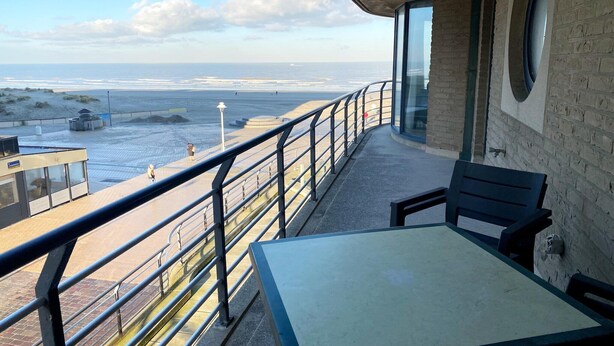 A balcony with a table and chairs overlooking the beach.